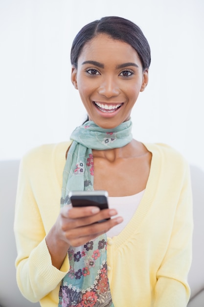 Souriante jolie femme assise sur le canapé SMS