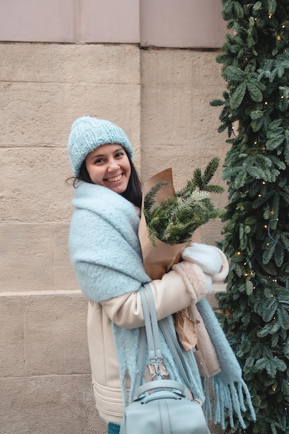 Souriante jolie femme marchant à l'extérieur tenant un bouquet de sapin de Noël