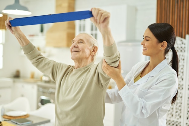 Souriante jolie infirmière aidant un homme âgé à faire des exercices à la maison