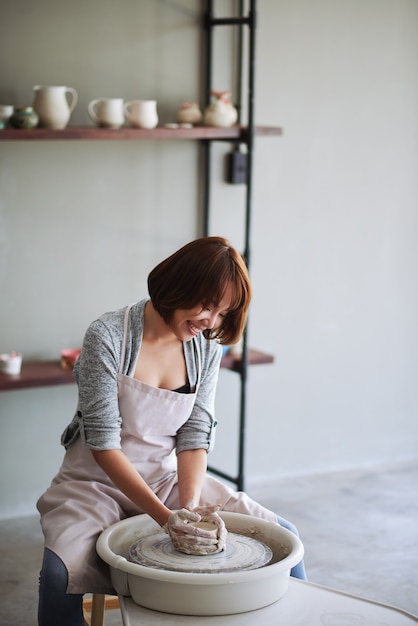 Souriante jolie jeune femme asiatique faisant un vase en argile ou un pot de fleurs à l'école de poterie