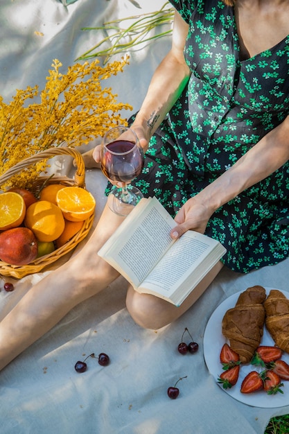 Souriante jolie jeune femme au chapeau et livre de lecture sur pique-nique dans le parc