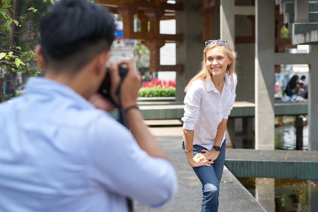 Souriante jolie jeune femme demandant à son petit ami de la photographier dans la rue