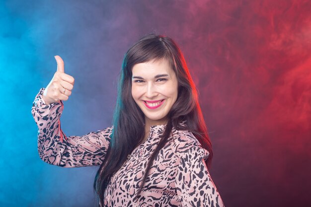 Souriante jolie jeune femme montrant le pouce vers le haut sur fond coloré