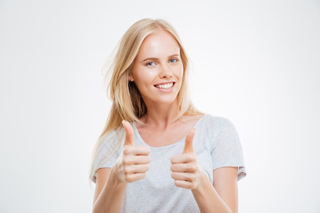 Souriante jolie jeune femme montrant les pouces vers le haut isolé sur le mur blanc