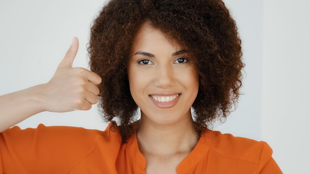 Photo souriante joyeuse femme heureuse afro-américaine avec une coiffure bouclée montrant le pouce vers le haut en regardant