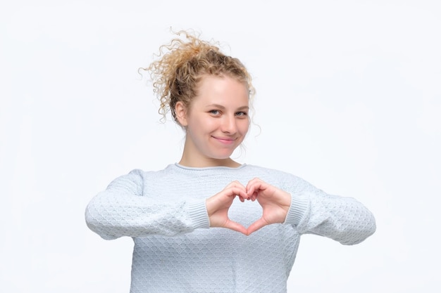 Souriante joyeuse jeune femme heureuse faisant signe de coeur avec les mains