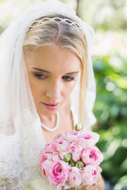 Photo souriante mariée portant le voile tenant le bouquet en regardant vers le bas