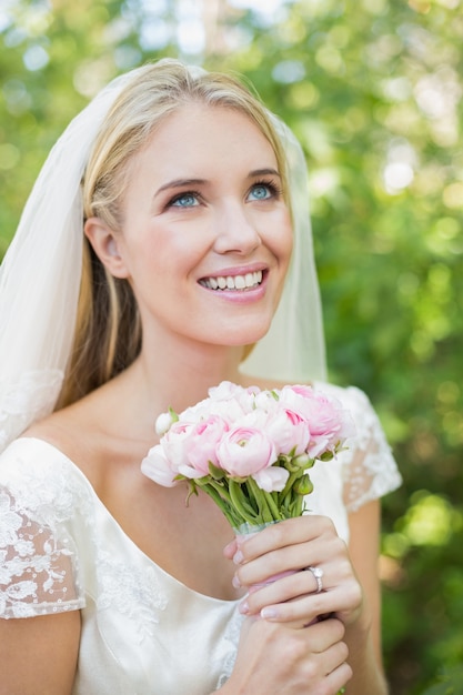 Photo souriante mariée tenant son bouquet portant un voile en levant