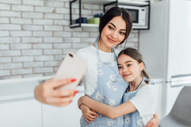 Souriante mère et fille prenant selfie dans la cuisine