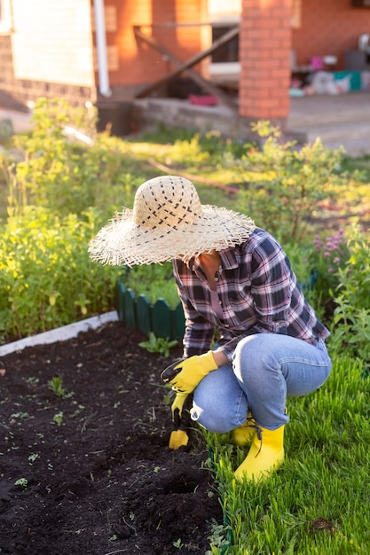 Souriante positive jeune femme jardinier plantes plantes dans le lit de jardin au printemps par une chaude journée ensoleillée. Concept d'agriculture biologique et de loisirs