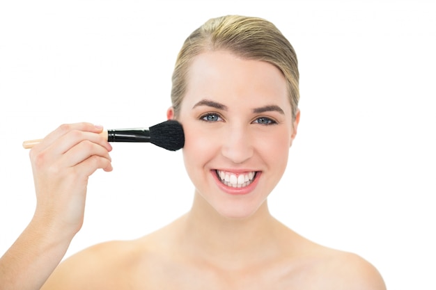 Souriante séduisante blonde à l&#39;aide de la brosse blusher