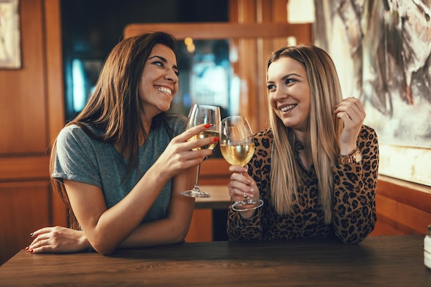 Souriantes jeunes amies chères sont assises dans le café, parlent, grillent et boivent du vin.