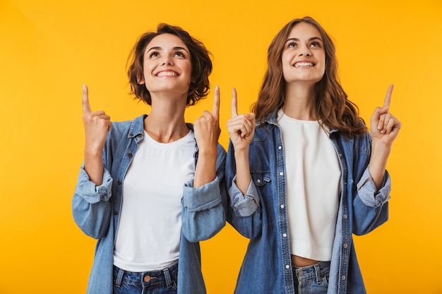 Sourire d'amis de jeunes femmes émotionnelles posant isolé sur mur jaune pointant.