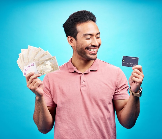 Sourire de l'argent et de la carte de crédit par un homme heureux en studio avec un financement de l'épargne ou une croissance des investissements sur fond bleu La joie de l'argent et un homme asiatique excité pour le succès bancaire ou la liberté financière isolés