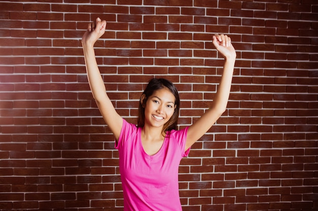 Sourire asiatique femme levant les bras sur le mur de briques