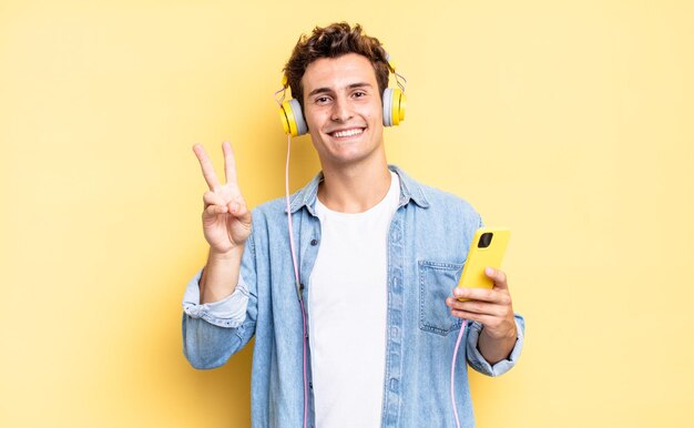 Sourire et avoir l'air heureux, insouciant et positif, gesticulant victoire ou paix d'une main. casque et concept de smartphone