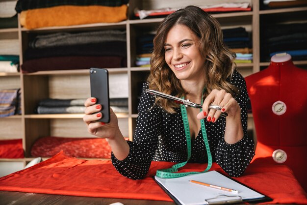 Sourire belle femme de couturière travaillant à l'atelier, prenant un selfie