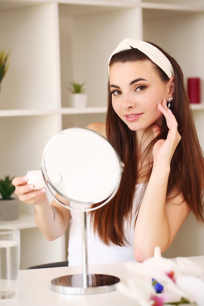 Sourire belle fille appliquer la crème pour la peau du visage pour se regarder dans le miroir.