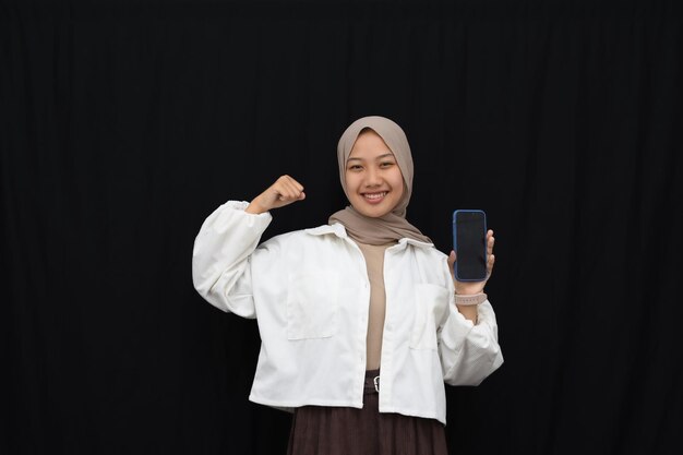 Sourire belle fille asiatique en hijab, montrant un écran vertical de téléphone portable vierge