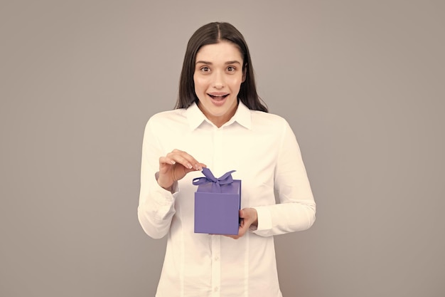 Sourire belle jeune femme brune en chemise tenir présent boîte avec noeud de ruban cadeau isolé sur fond gris clair studio portrait concept d'anniversaire
