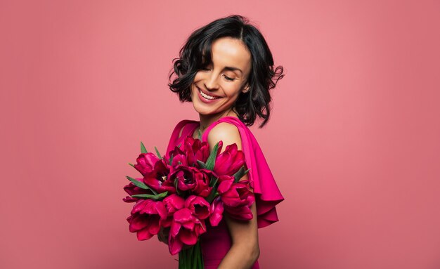 Sourire charmant. Photo en gros plan d'une fille ravie déguisée, qui tient un bouquet de tulipes et la regarde avec un large sourire.