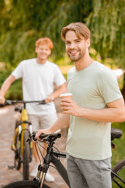 Sourire content bel homme sportif barbu avec un gobelet en papier jetable et son ami aux cheveux roux en arrière-plan