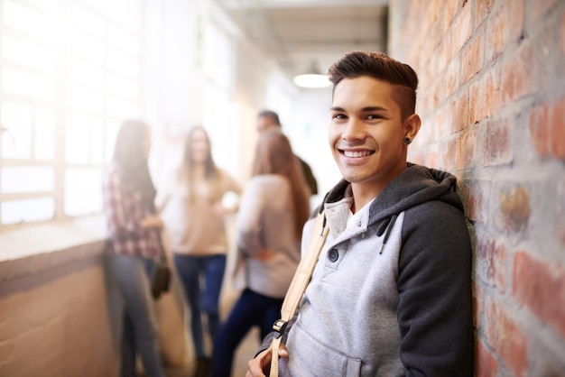 Sourire de l'éducation et portrait d'un homme dans le couloir du collège pour étudier l'apprentissage et l'érudition Futur heureux et connaissance avec l'étudiant se détendre sur le mur de briques pour l'académie universitaire et le campus