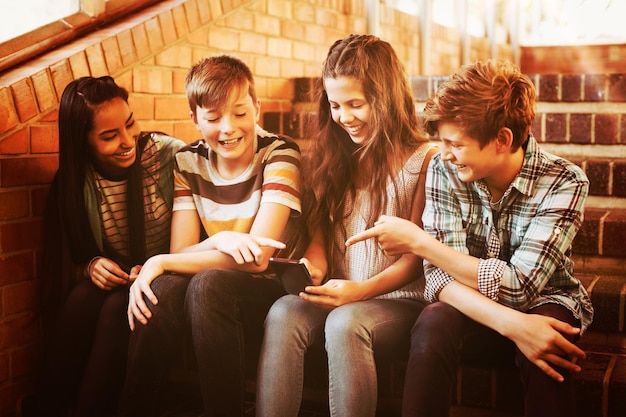 Sourire des élèves de l'école assis sur l'escalier à l'aide d'un téléphone mobile