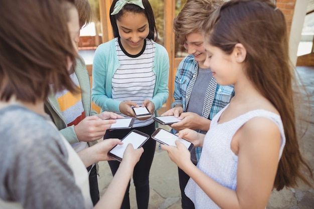 Photo sourire des élèves de l'école debout en cercle et à l'aide de téléphone mobile