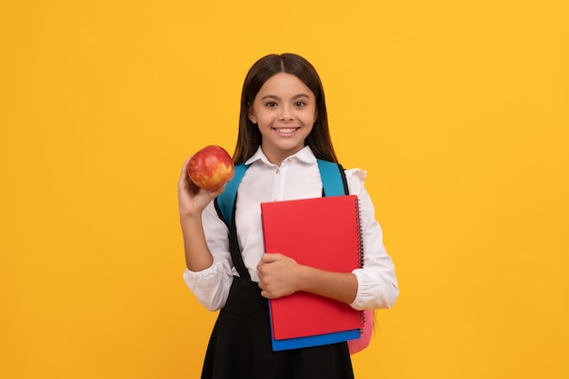 Sourire enfant fille heureuse tenant pomme et livres fond jaune, école