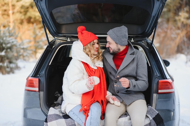 Sourire ensemble. Un beau couple passe un week-end à la campagne en hiver. Assis sur la partie arrière de la voiture moderne.