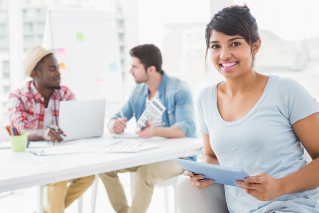 Sourire de femme d&#39;affaires tenant la tablette sur le canapé avec des collègues derrière elle