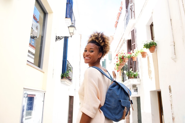 Sourire de femme africaine marchant dans la rue étroite avec un sac