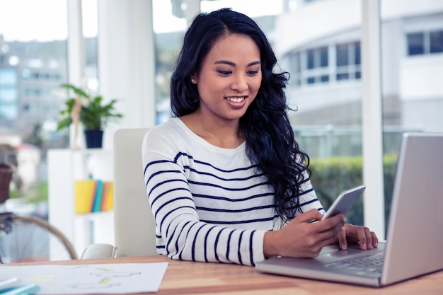 Sourire de femme asiatique à l&#39;aide de smartphone et ordinateur portable au bureau