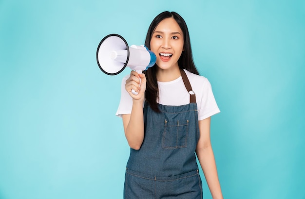 Sourire femme asiatique tenant un mégaphone avec les poings serrés célébrant la victoire exprimant le succès sur fond bleu.