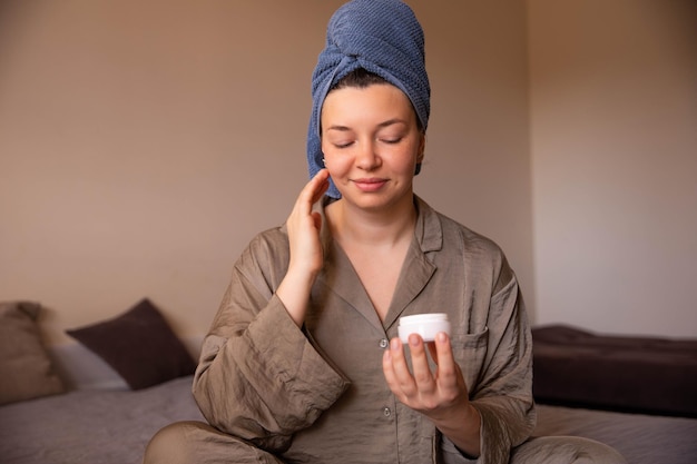 Photo sourire femme avec de la crème pour le visage vue rapprochée à la maison regarder la crème