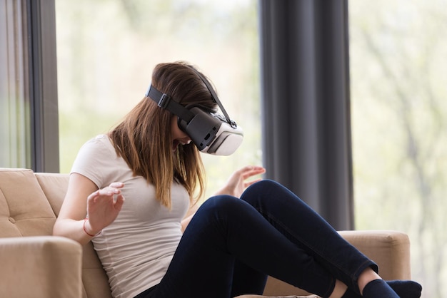 Sourire une femme heureuse qui acquiert de l'expérience en utilisant des lunettes de réalité virtuelle à casque VR à la maison