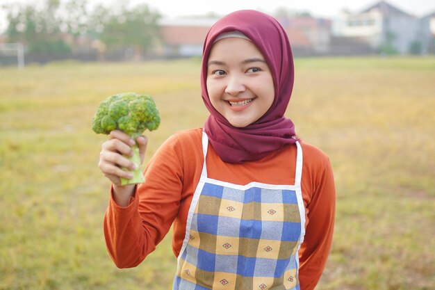 Photo sourire de femme hijab asiatique portant un tablier tenant des légumes