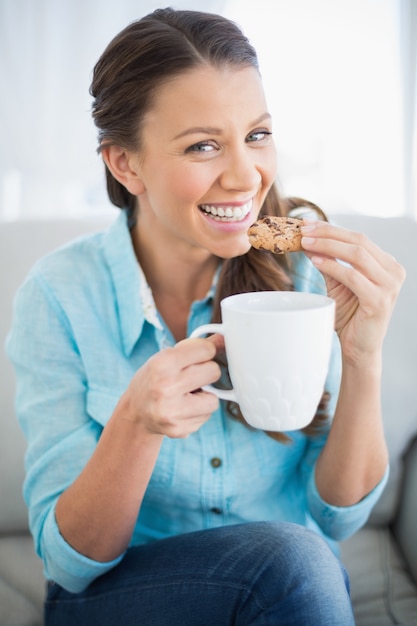 Sourire femme manger cookie tenant une tasse de café