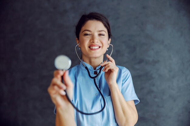 Sourire femme médecin tenant le stéthoscope vers la caméra comme elle examine les poumons.