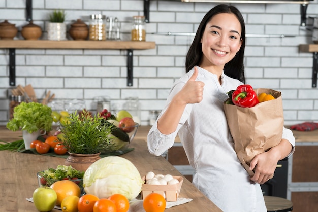 Sourire femme montrant le pouce en haut signe tout en maintenant le sac d&#39;épicerie brun