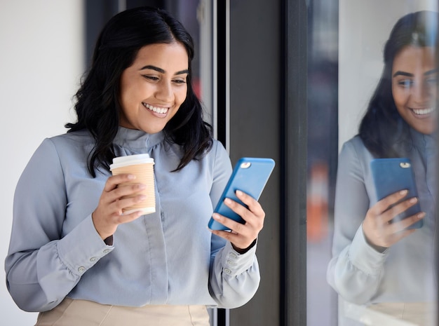 Sourire femme avec téléphone au bureau pendant la pause-café en parcourant les médias sociaux en surfant sur Internet ou en tapant un message Communication technologique et femme d'affaires heureuse debout dans le hall lisant sur smartphone