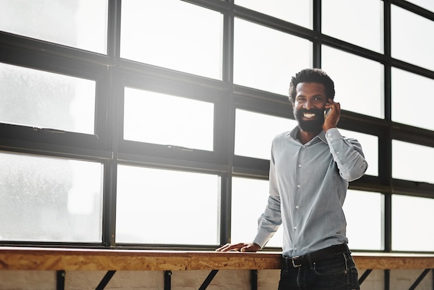 Sourire de fenêtre et appel téléphonique avec un homme d'affaires parlant au bureau tout en réseautant pour la négociation Mobile heureux et communication avec un employé masculin heureux debout au travail pendant sa pause