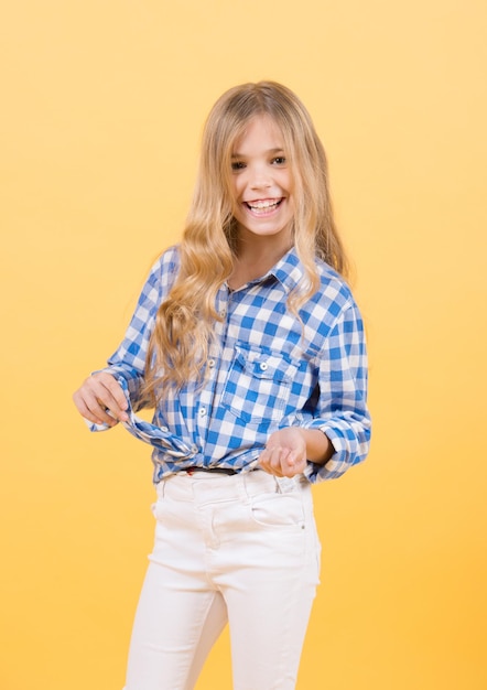 Sourire de fille en chemise à carreaux bleue et pantalon blanc