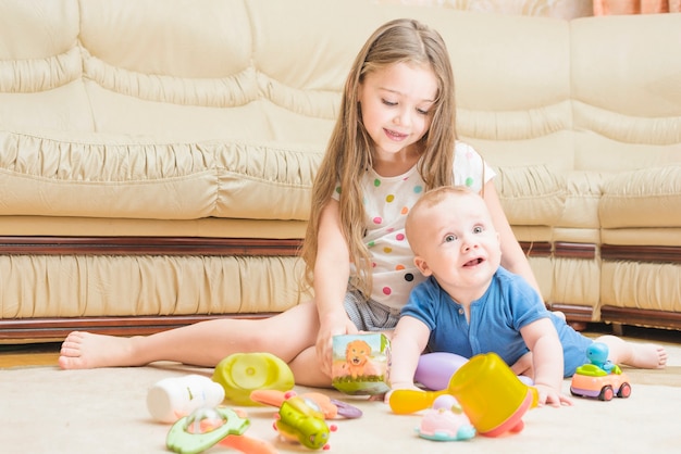 Sourire fille jouant avec son bébé frère sur tapis