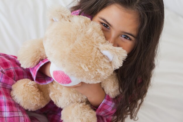 Sourire fille avec peluche assis sur le lit