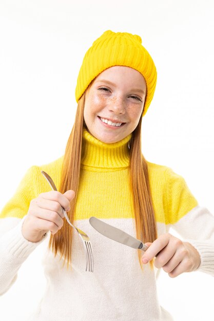 Sourire de fille rousse européenne tenant une fourchette et un couteau sur blanc