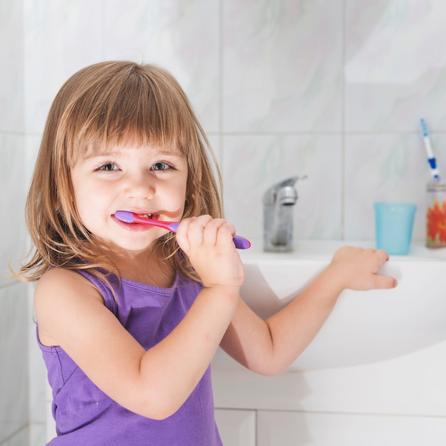 Sourire fille tenant la brosse à dents debout devant le lavabo