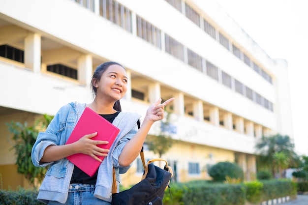 Sourire fille tenir livre rose debout sur fond de bâtimentRetour à l'école