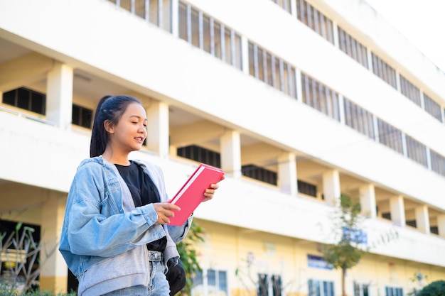 Sourire fille tenir livre rose debout sur fond de bâtimentRetour à l'école